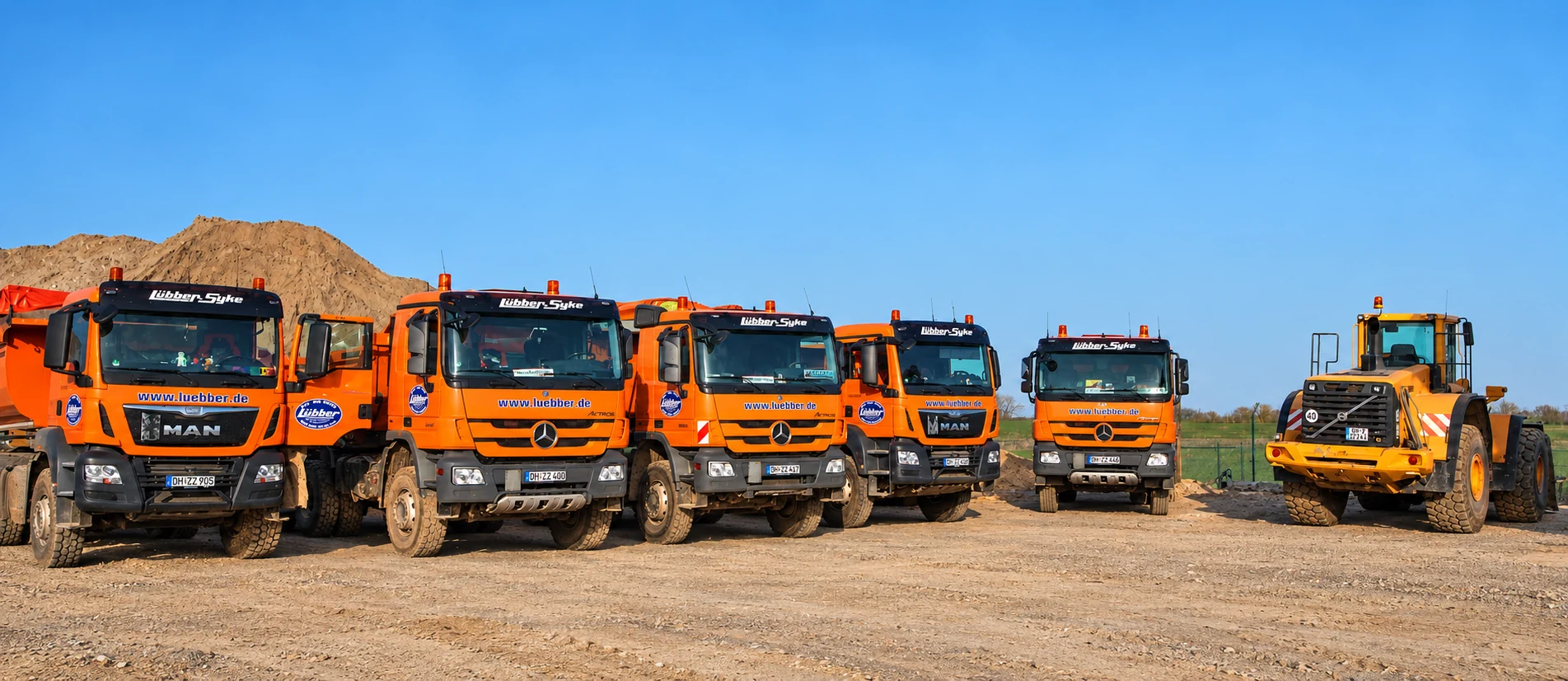 Lübber-Fuhrpark mit Lkw und Radlader; unterer Bildbereich mit Rädern und Boden per KI ergänzt